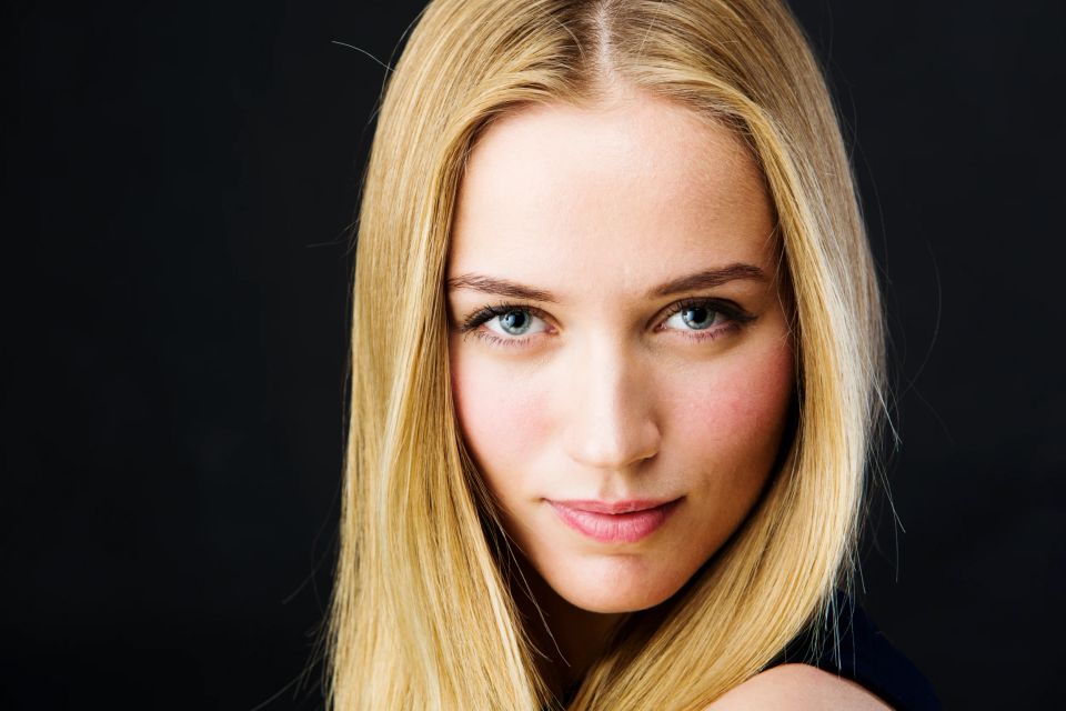 Nærbillede portrætfoto af blond kvinde med strålende blå øjne og blødt lys mod mørk baggrund.