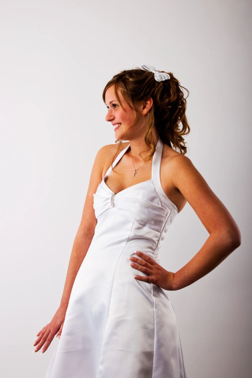 Portrætfoto af smilende ung kvinde i hvid gallakjole med lyst opsat hår, der kigger mod højre i blødt lys.