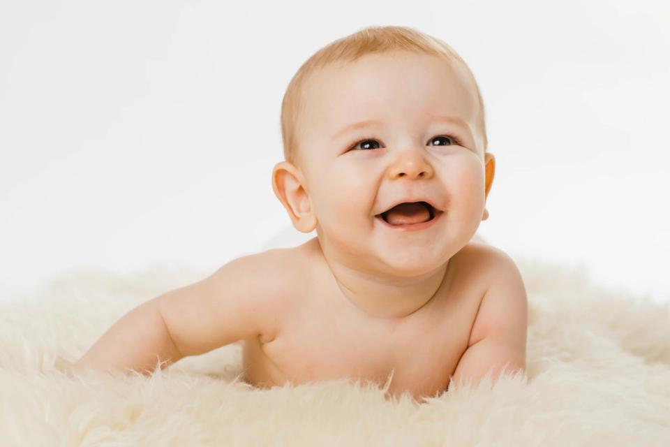 Glad baby ligger på lyst fåreskind, smilende med åben mund og ser op. Et hjertevarmt babyfotografi.
