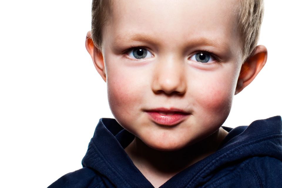 Børnefoto: Nærbillede af smilende dreng med glimt i øjet og rød kinder iført mørkeblå hættetrøje.