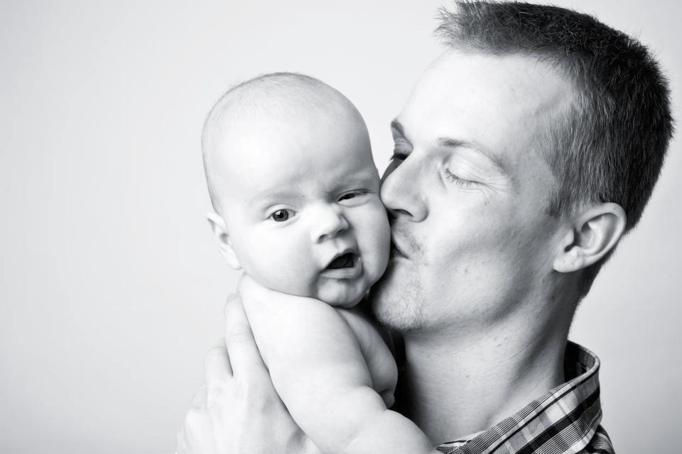 Sort-hvidt babyfotografi af far, der kysser sin baby på kinden, skaber et ømt og intimt øjeblik.
