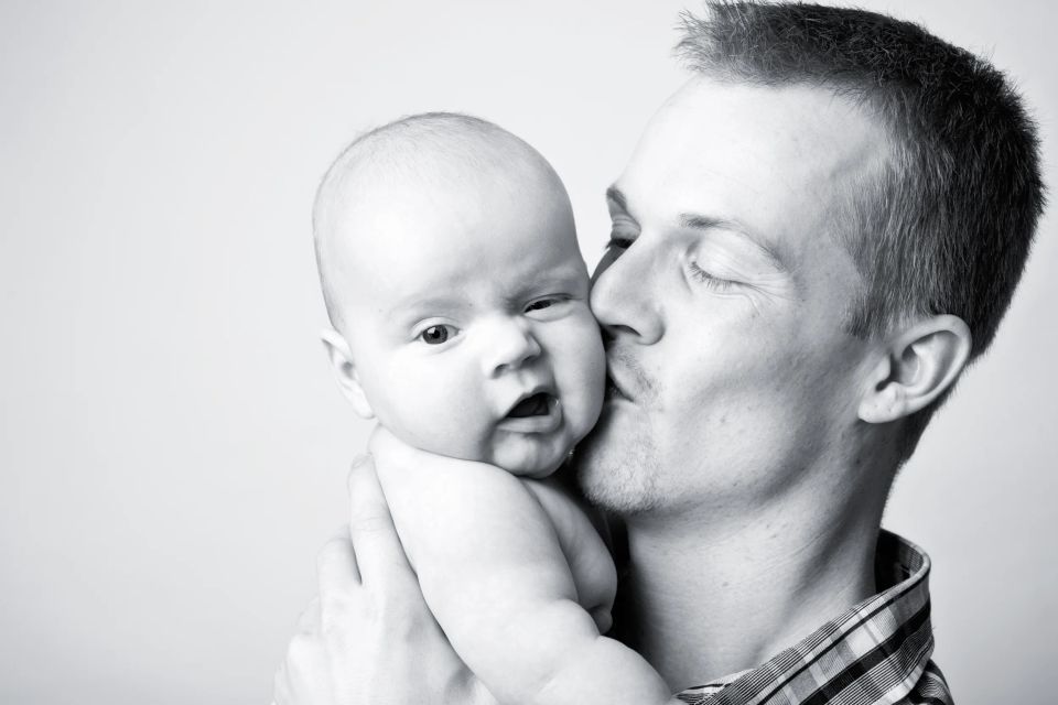 Sort-hvidt babyfotografi af far, der kysser sin baby på kinden, skaber et ømt og intimt øjeblik.