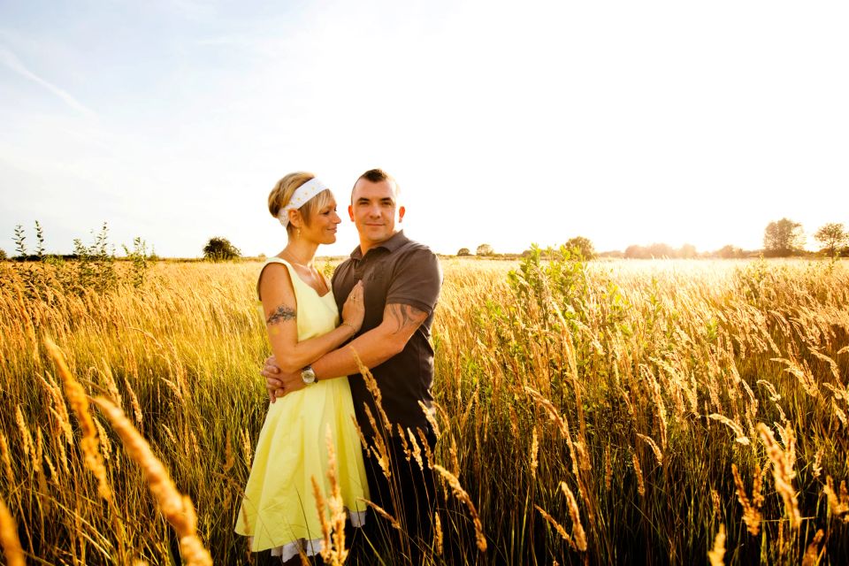 Portrætfoto af et forelsket par der omfavner hinanden i et gyldent kornfelt i varmt, naturligt lys fra siden.