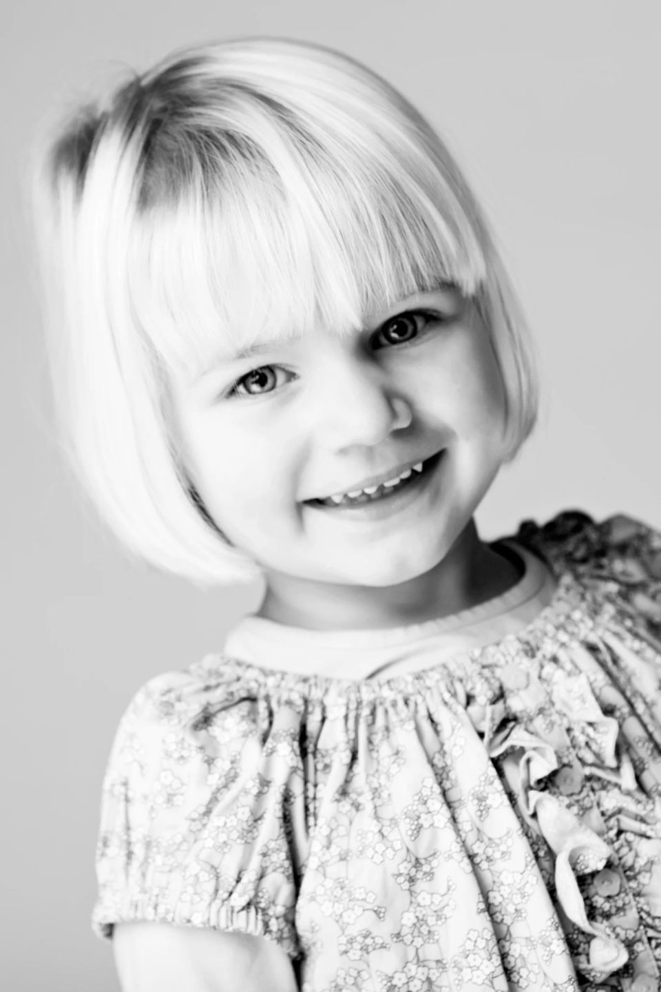 Nærbillede af smilende lyshåret pige i sort-hvid. Børnefotografi af glad pige med skuldrene skråt mod kameraet.