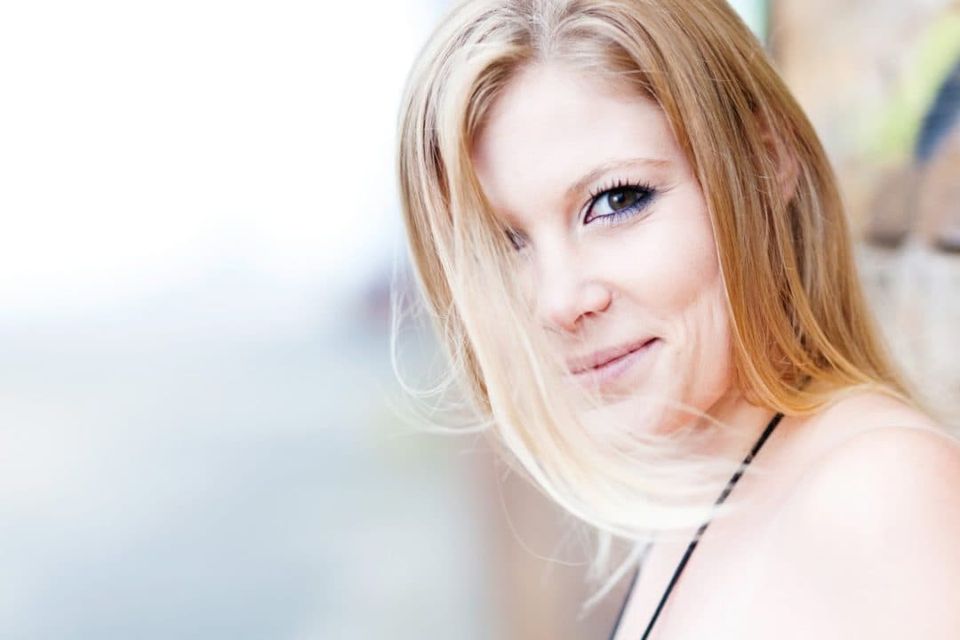 Nært portrætfoto af en blond kvinde med et ægte smil, der kigger ind i kameraet med blødt lys.