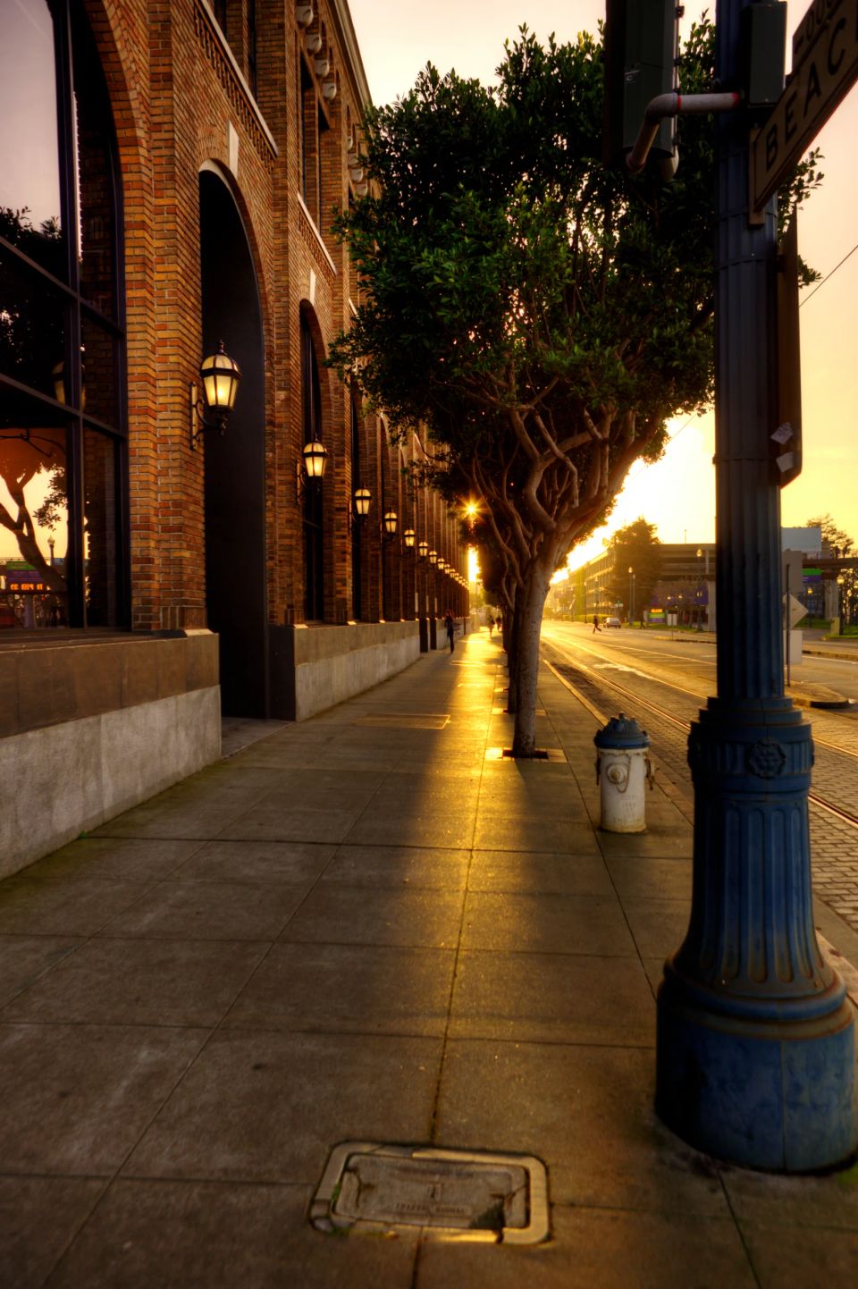 Fortov belyst af varmt, guldgyldent dagslys langs en murstensbygning med lyse lanterner og træer mod en vej.