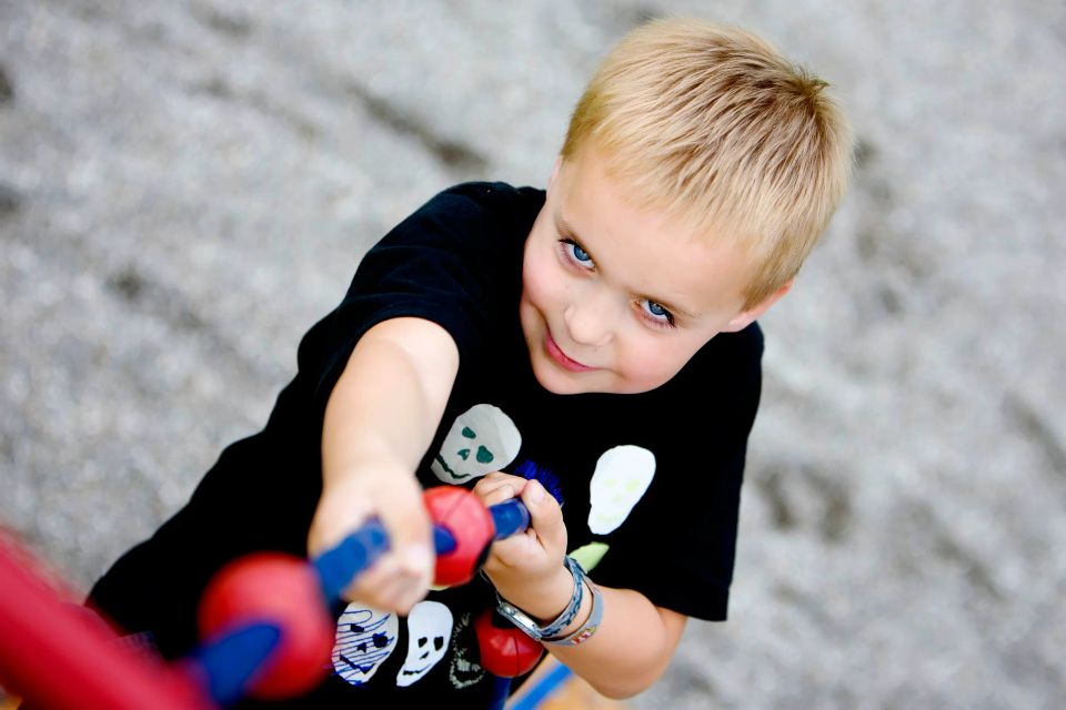 Billede af legende barn med blond hår og blå øjne. Barnet ses i et naturligt, smilende øjeblik med legetøj.