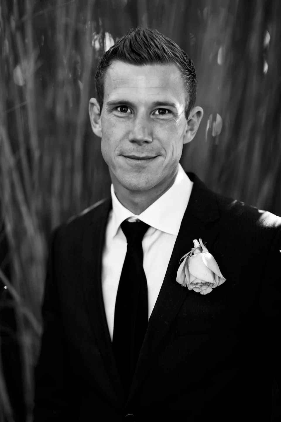 Bryllupsbillede af smilende mand i sort jakkesæt med hvid skjorte og reversnål, taget i Virum i et naturligt dagslys.