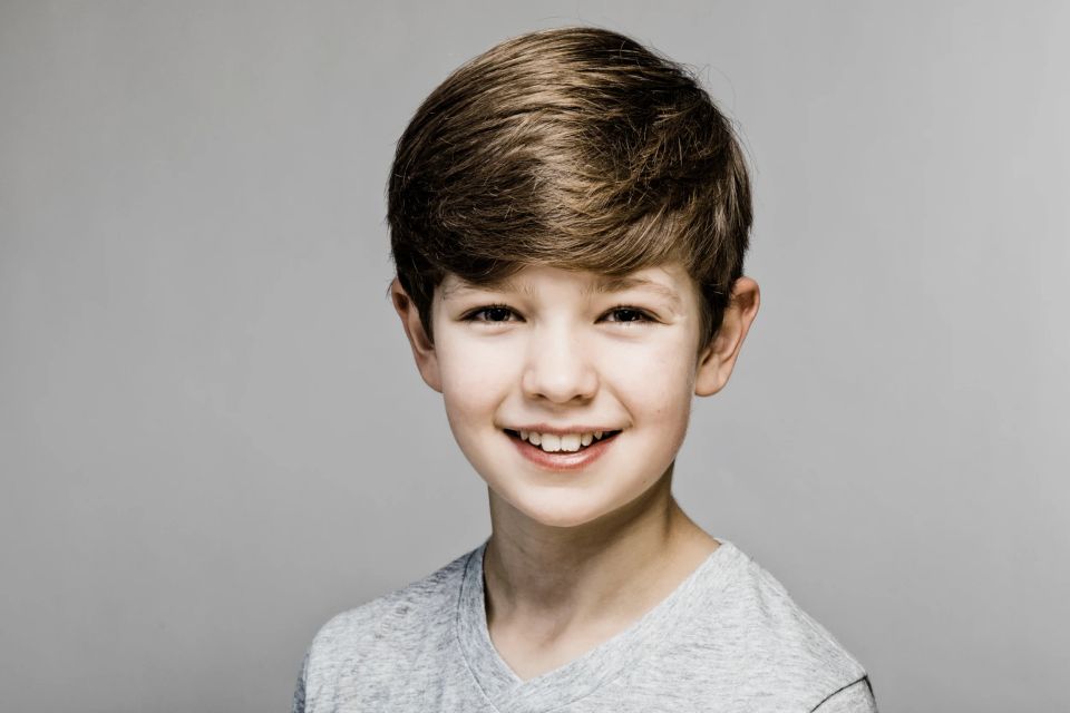 Nærbillede af glad dreng med smil og brunt hår, naturligt børneportræt med blød belysning i Virum. Fotografering af børn.