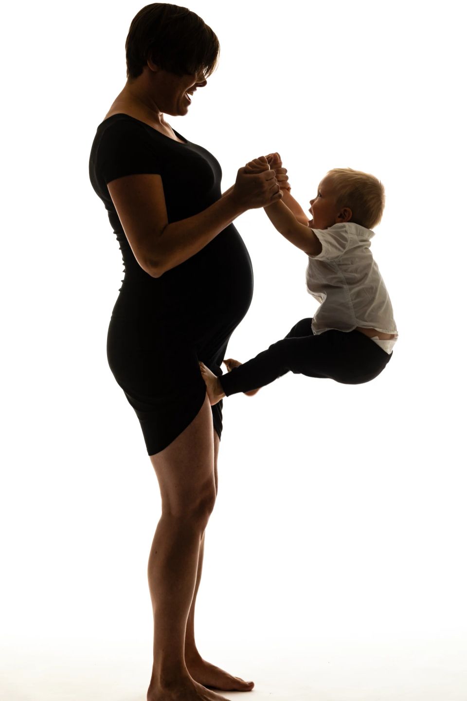 Gravidfotografering: Silhuet af en smilende gravid mor der holder et barn legende op i luften, sort/hvidt billede.