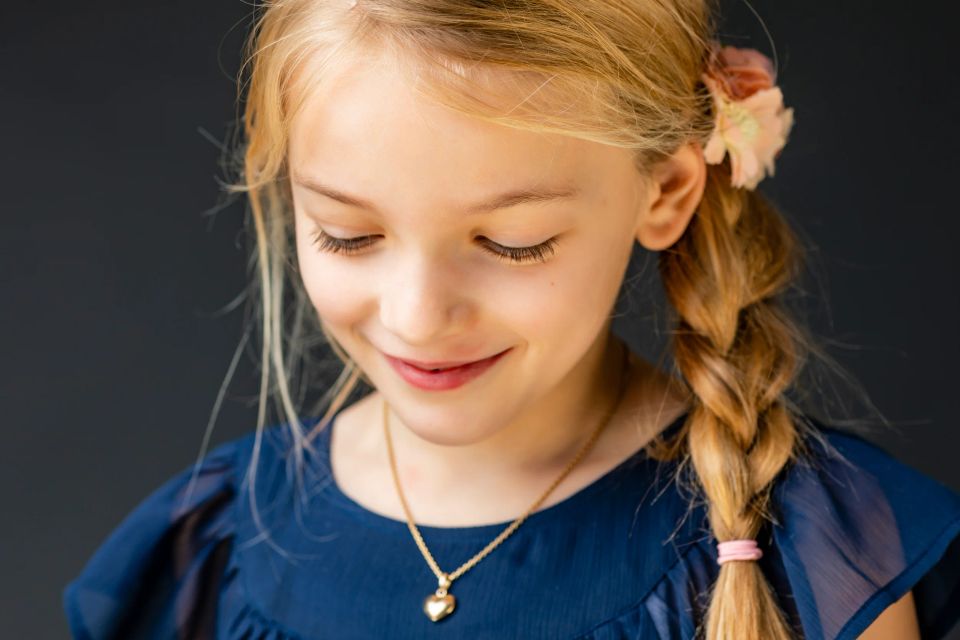 Nært portrætfoto af ung pige med blondt flet, smilende med lukkede øjne i blødt lys, iført blå kjole.