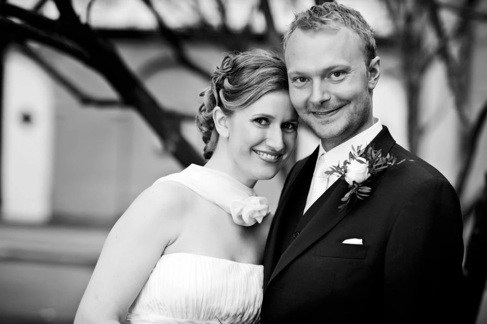 Bryllupsfoto af smilende par, kvinden i hvid brudekjole, manden i sort jakkesæt, i et ægte og kærligt øjeblik.