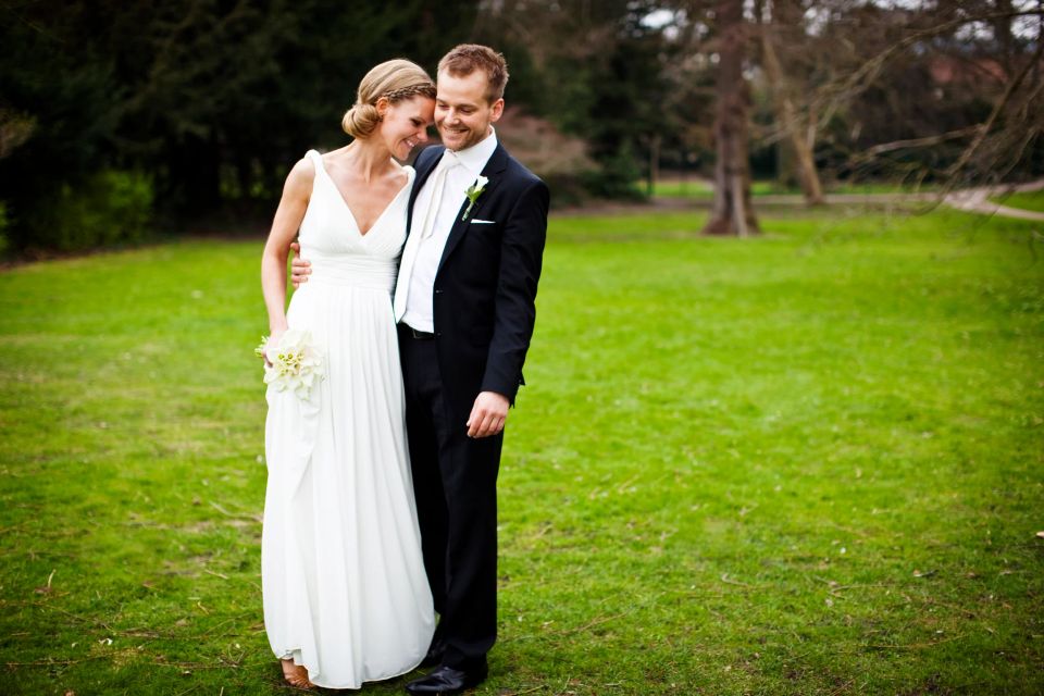 Bryllupsfotografering af smilende brudepar i græsset, bruden med armen om gommen, i naturligt lys