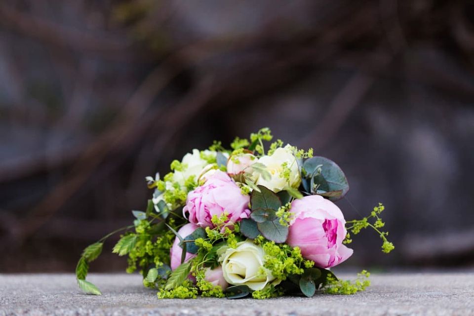Bryllupsfotografi af brudebuket med lyserøde pæoner og hvide roser på en grå stenoverflade