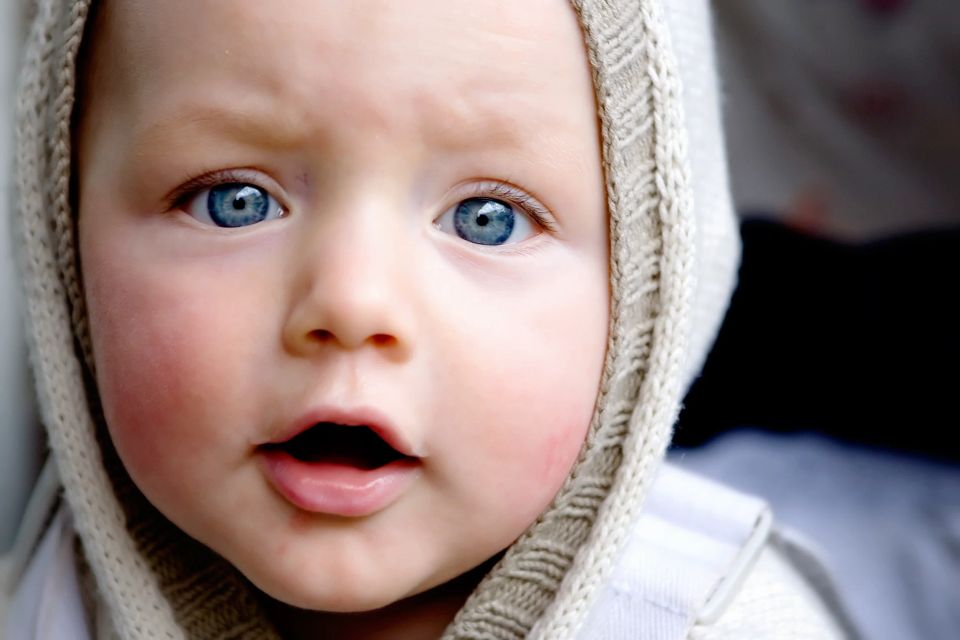 Nærbillede af baby med store blå øjne og åben mund, iført en strikhue, som et sødt baby Virum foto.