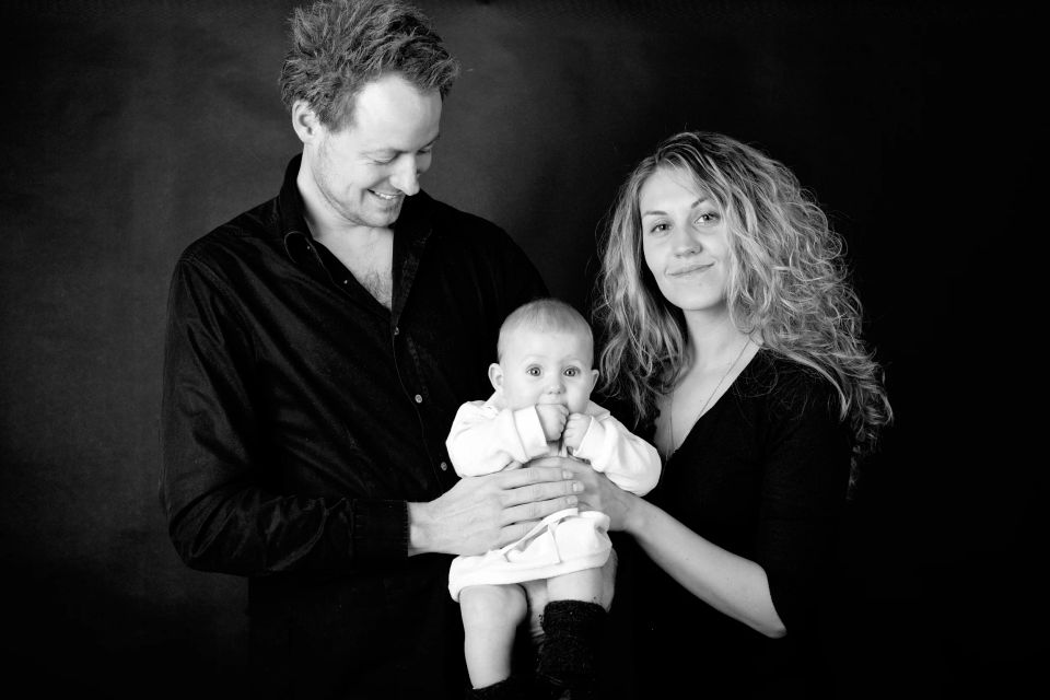 Familiefotografering: Sort/hvidt billede af smilende forældre, der holder deres baby mod mørk baggrund.