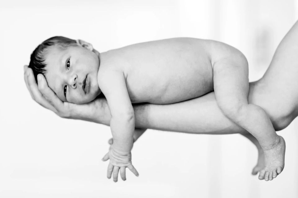 Sort/hvidt babyfotografi: En nøgen, sovende baby holdes trygt i en voksens hånd. Blødt naturligt lys.