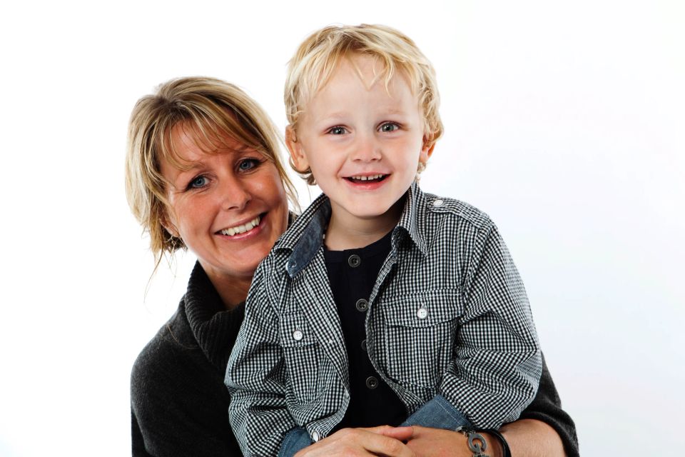 Glad mor med lyst hår holder sit smilende barn. Familie fotografering med fokus på ægte glæde.