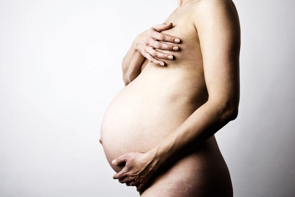 Gravid fotografering. En ventende mor holder sine hænder beskyttende på sin gravide mave og over brystet. Smuk stemning.