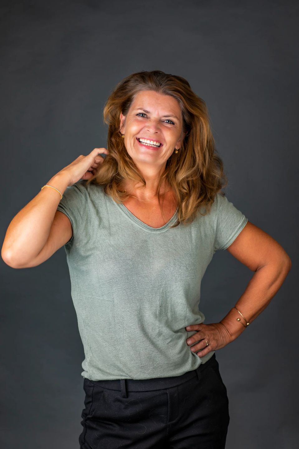 Glad kvinde med smil i ansigtet, grønt tøj og brunt hår foran grå baggrund, et charmerende portrætfoto.