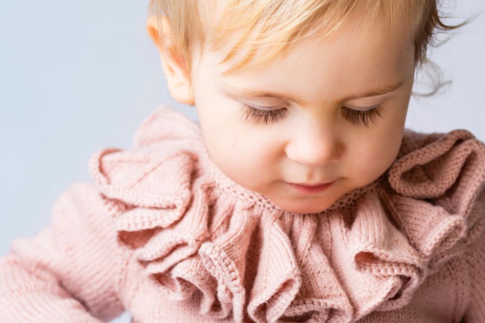 Nærbillede af et roligt barn i en lyserød striktrøje med flæser, der kigger nedad i naturligt lys. Børnefotografering.