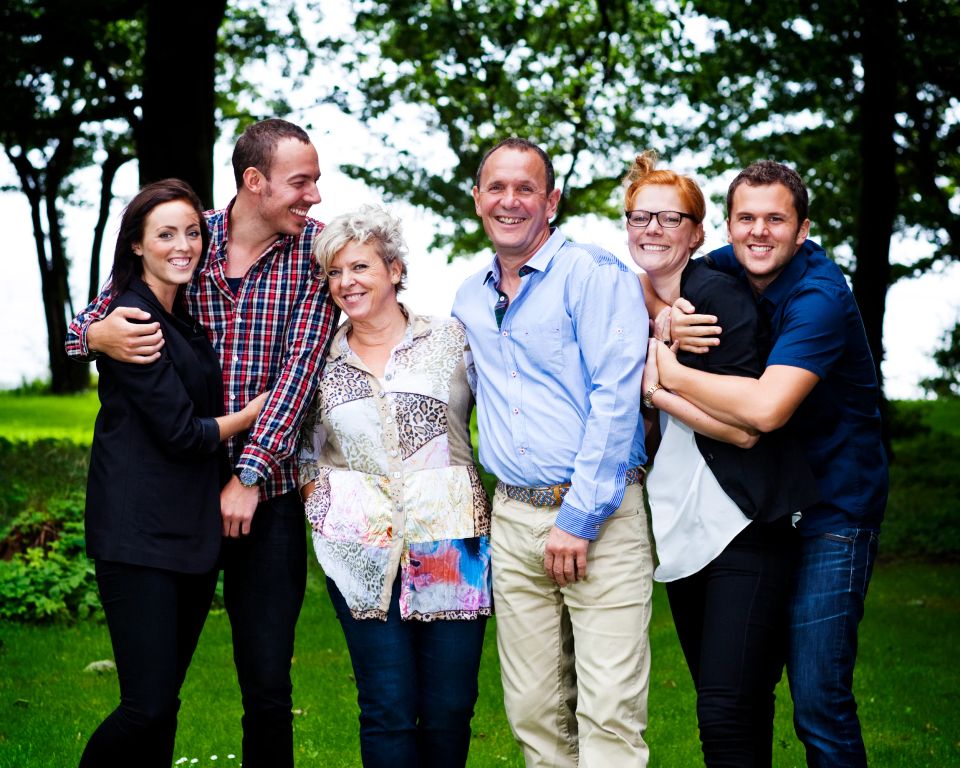 Glad familiefotografering med fem smilende personer stående i tæt gruppe udendørs i grøn natur i Virum.