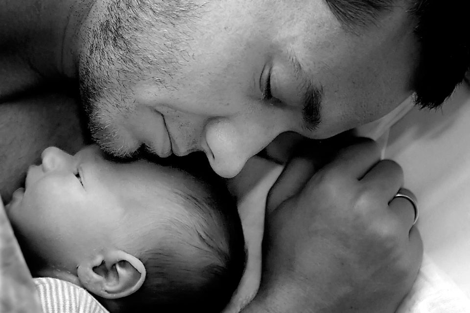 Nært familiefoto i sort/hvid af far, der kysser sit sovende spædbarn på panden, skaber en øm stemning.