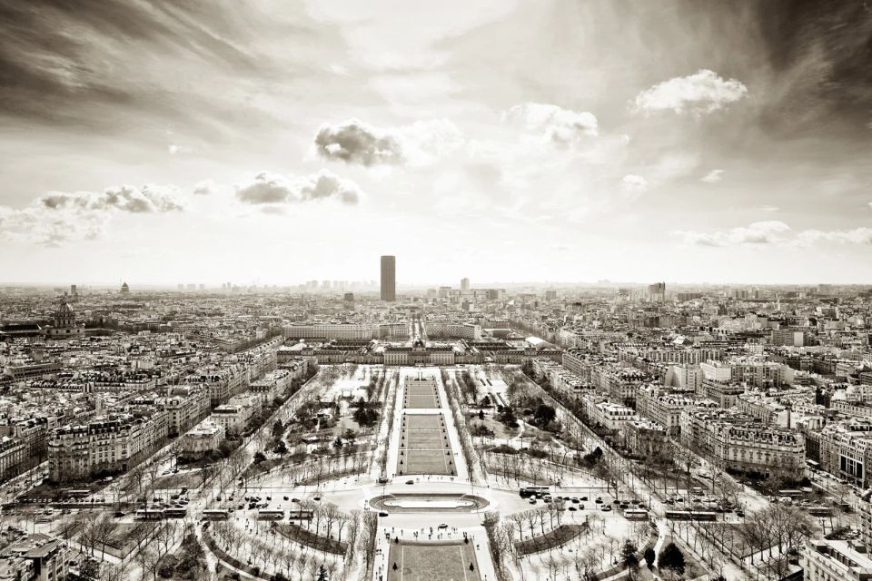 Oversigtsfoto af Paris i sepia nuancer, med grønne alléer og byens tage under en skyet himmel. Stemningsfuldt. Andet foto.