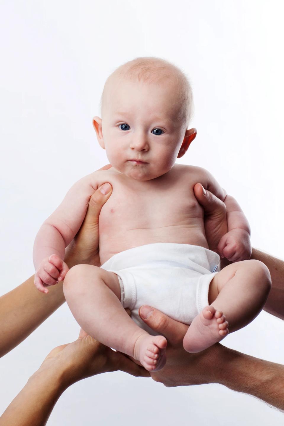 Babyfotografering: Et lille barn holdes nænsomt af voksne hænder mod hvid baggrund, skaber en følelse af tryghed.
