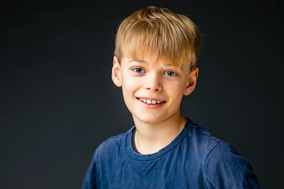 Børnefotografering: Smilende dreng med lyst hår og blå øjne i blødt lys, iført blå t-shirt.