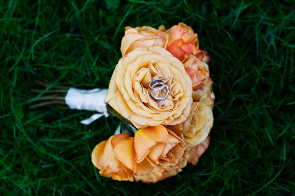 Bryllupsbillede med guldbryllupsringe på en brudebuket med smukke orangerøde roser på en grøn græsplæne.