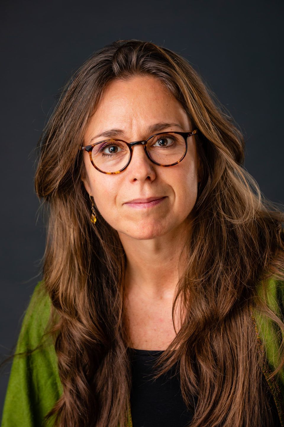 Portrætfoto af kvinde med brunt hår og fine briller, direkte blik, blød belysning skaber en intim stemning.