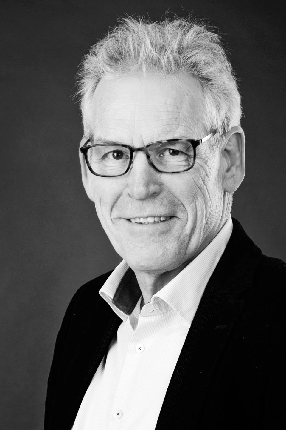 Nærbillede i sort/hvid af smilende ældre mand med briller og gråt hår i et venligt portrætfoto.