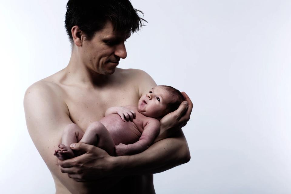 Babyfotografering hvor en far kærligt holder sin nyfødte baby, begge badet i blødt sidelys. Kæmpe samhørighed.