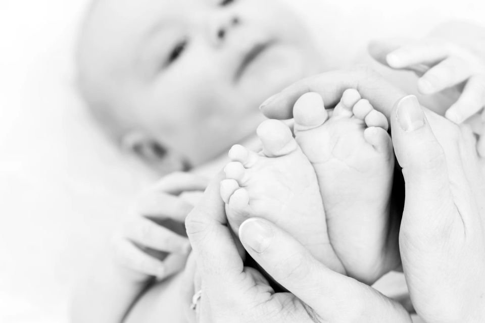 Forældrehånd holder forsigtigt en babys små fødder i et nært sort-hvidt foto der understreger ømhed og tryghed.