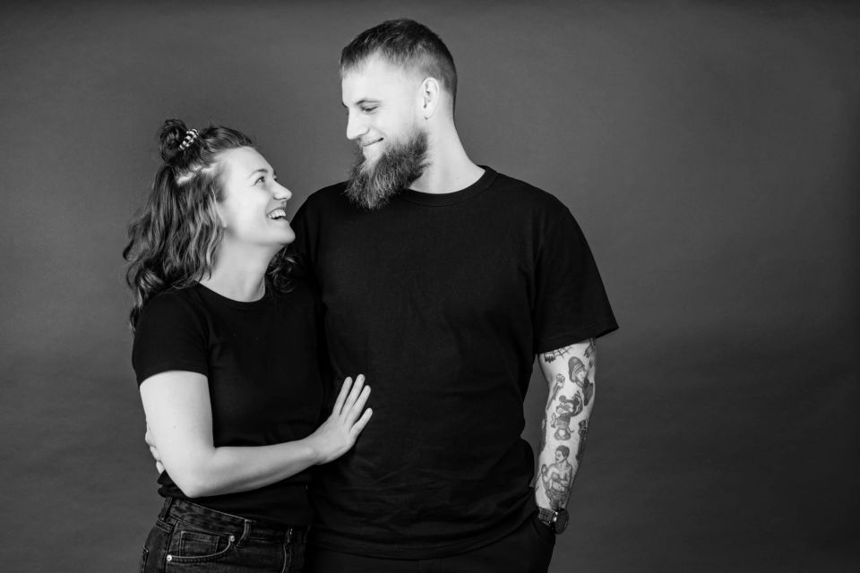 Sort-hvidt portrætbillede af smilende kærestepar. Kvinden med krøllet hår kigger forelsket op på manden med skæg.