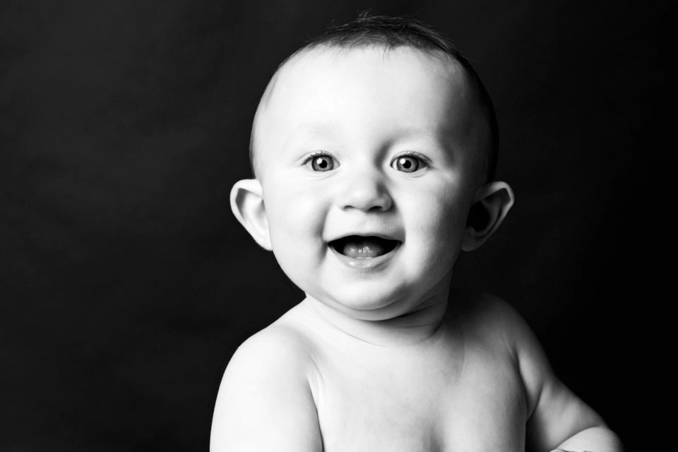 Sort/hvid babyfoto af legende baby med åben mund og store øjne, der smiler spontant mod beskueren.