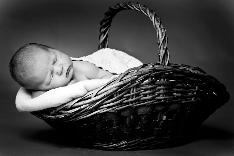 Sort-hvidt babyfoto af sovende baby i fletkurv med hvidt tæppe i blødt sidelys. Fredfyldt. Babyfotografering.