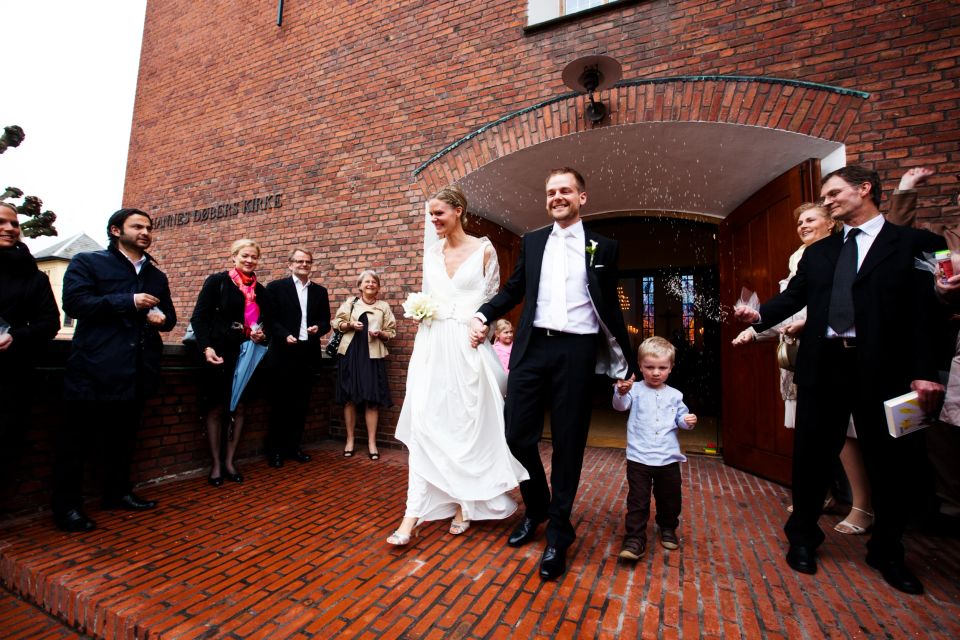 Bryllupsfoto af smilende brudepar hånd i hånd, dækket af risregn, forlader kirke