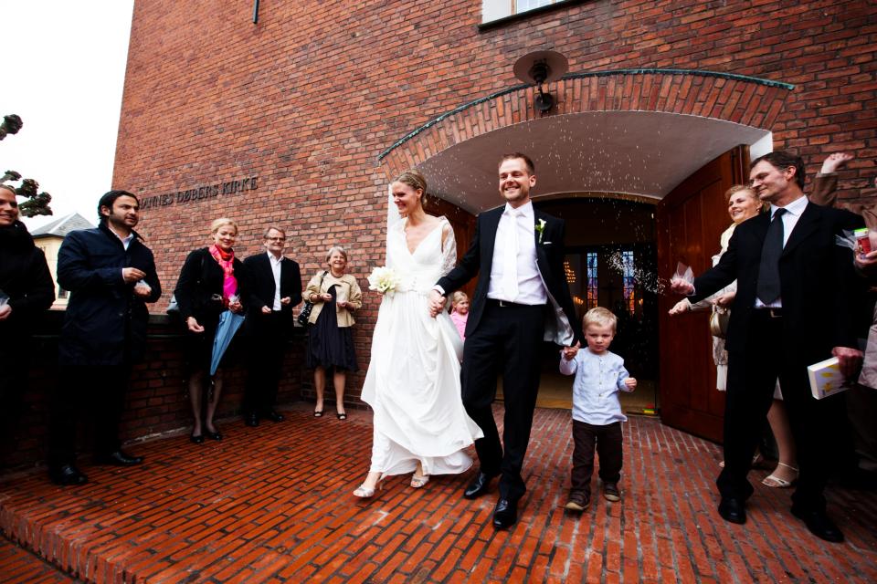 Bryllupsfoto af smilende brudepar hånd i hånd, dækket af risregn, forlader kirke