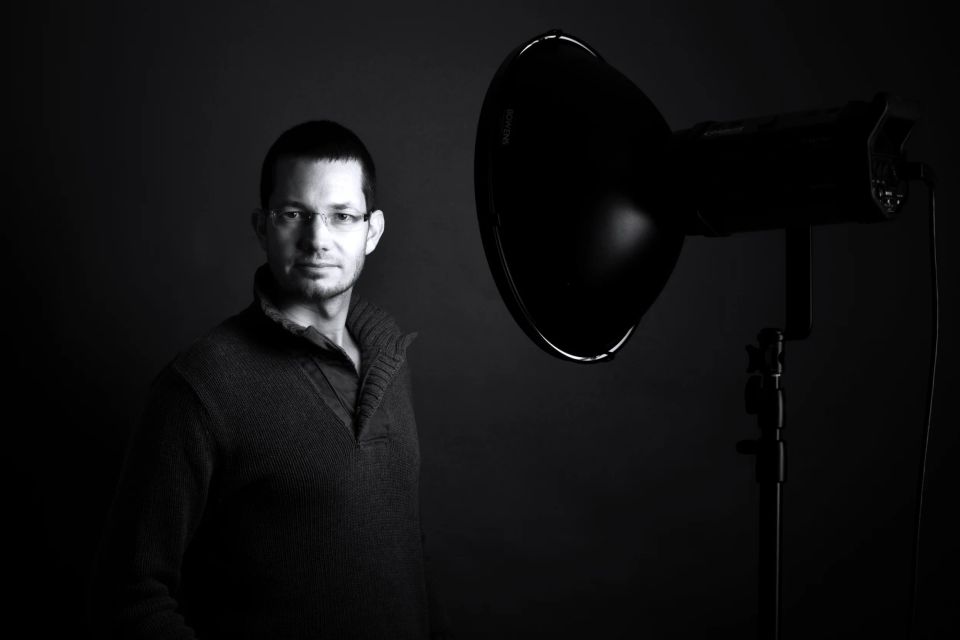 Professionelt sort-hvid portrætfoto af en mand med briller, der ser direkte ind i kameraet med et studieflash til højre.