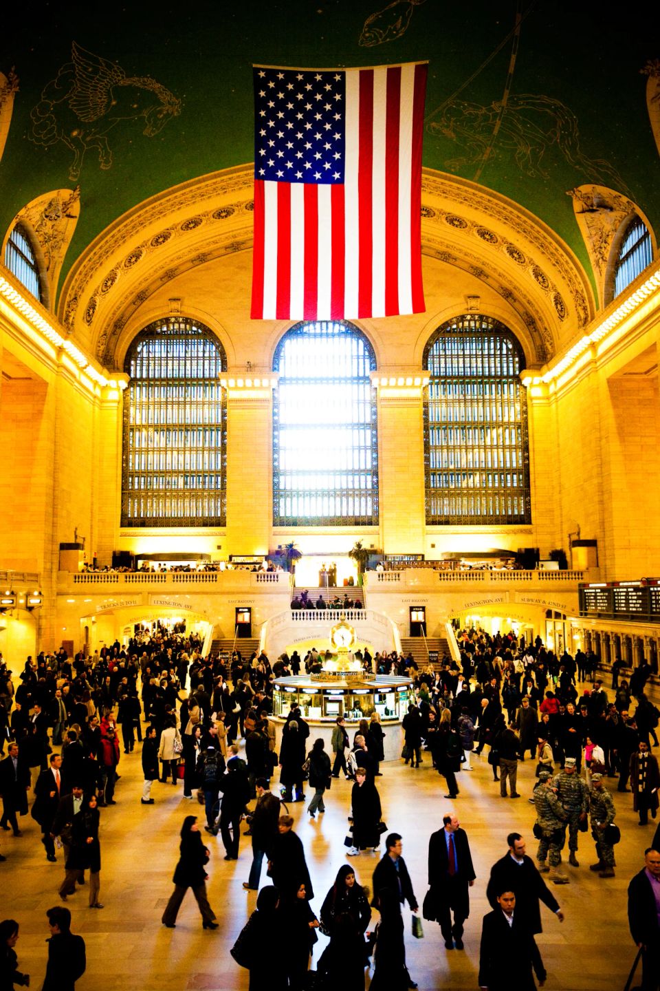 Amerikansk flag hænger over den travle Grand Central Terminal i New York, fyldt med gule lys og et væld af mennesker. Ande...