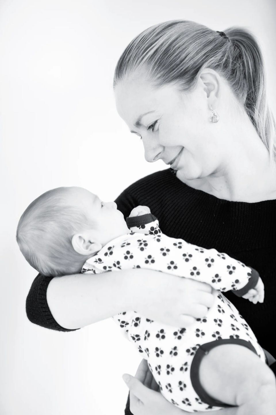 Baby fotografering: Sort-hvidt foto af en mor, der holder sin baby tæt i favnen med øjenkontakt og store smil.
