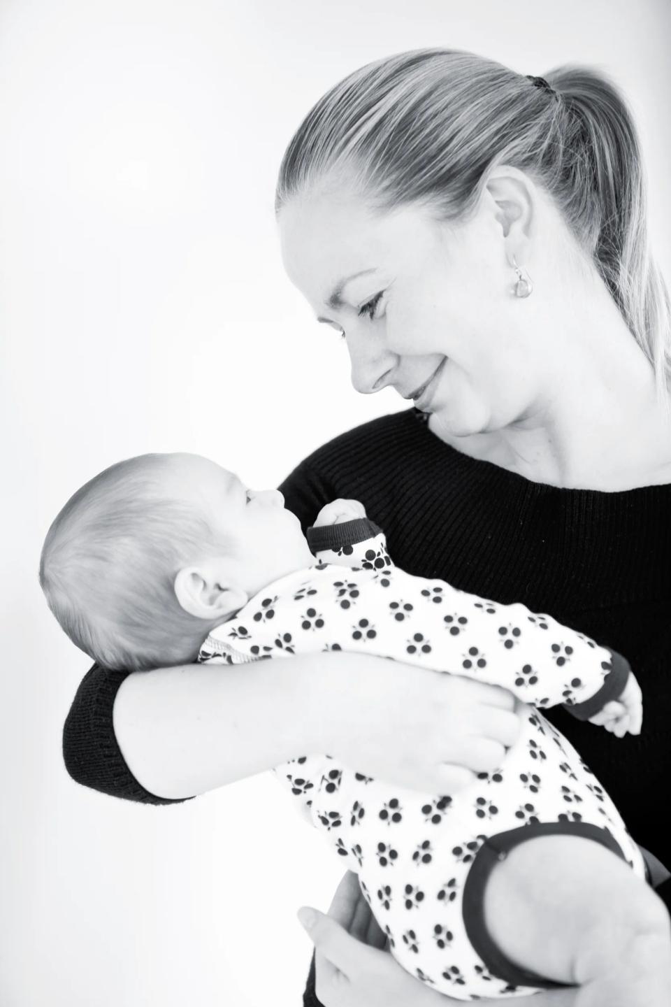 Baby fotografering: Sort-hvidt foto af en mor, der holder sin baby tæt i favnen med øjenkontakt og store smil.