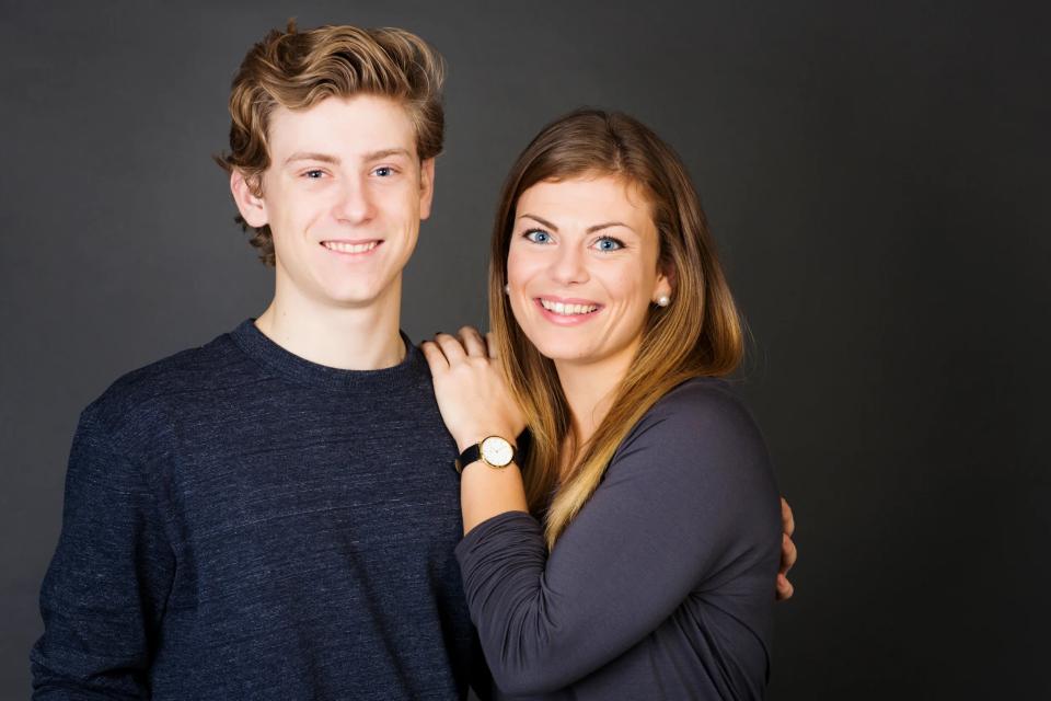 Familiefoto af søskende. En ung kvinde med brunt hår og blå øjne smiler og holder armen om en ung mand.