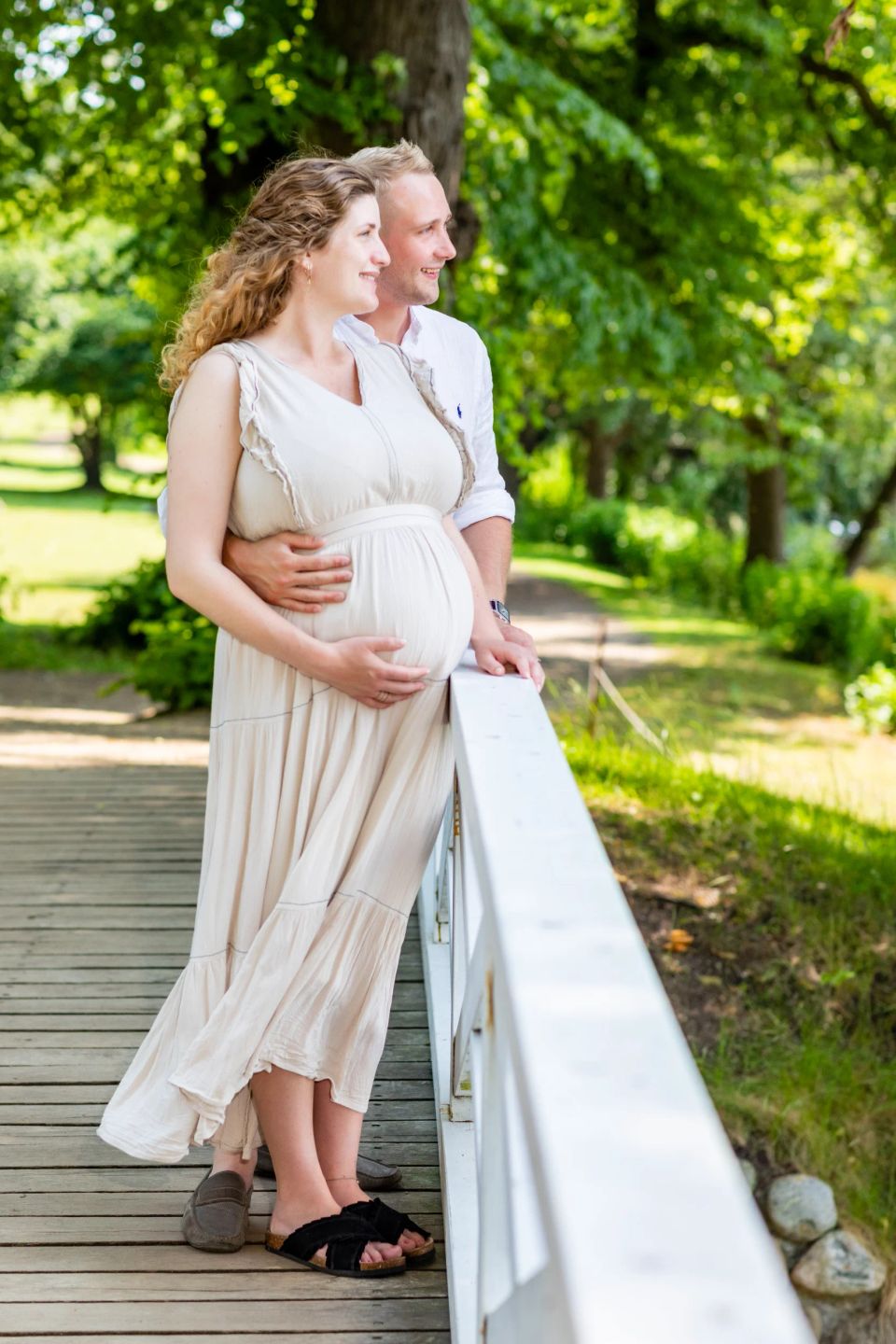 Gravidfotografi af forventningsfuldt par på træbro i Virum; manden holder om kvindens gravide mave i naturligt lys.