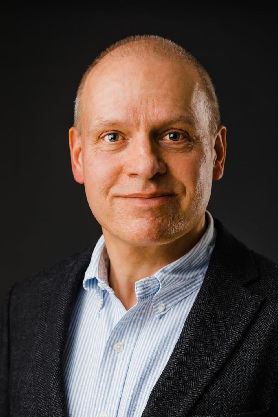 Portrætfoto af mand med sparsomt hår, i gråt sildebensmønstret jakkesæt og lyseblå skjorte, ser ægte mod kameraet.