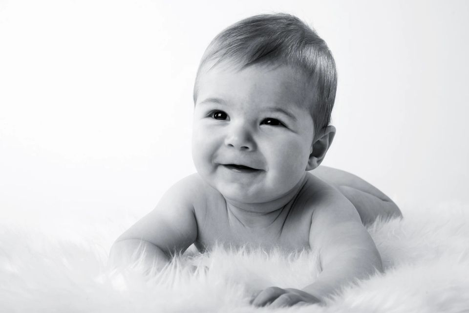 Glad, smilende baby i sort/hvid liggende på maven på et blødt, hvidt tæppe. Et dejligt babyfoto.
