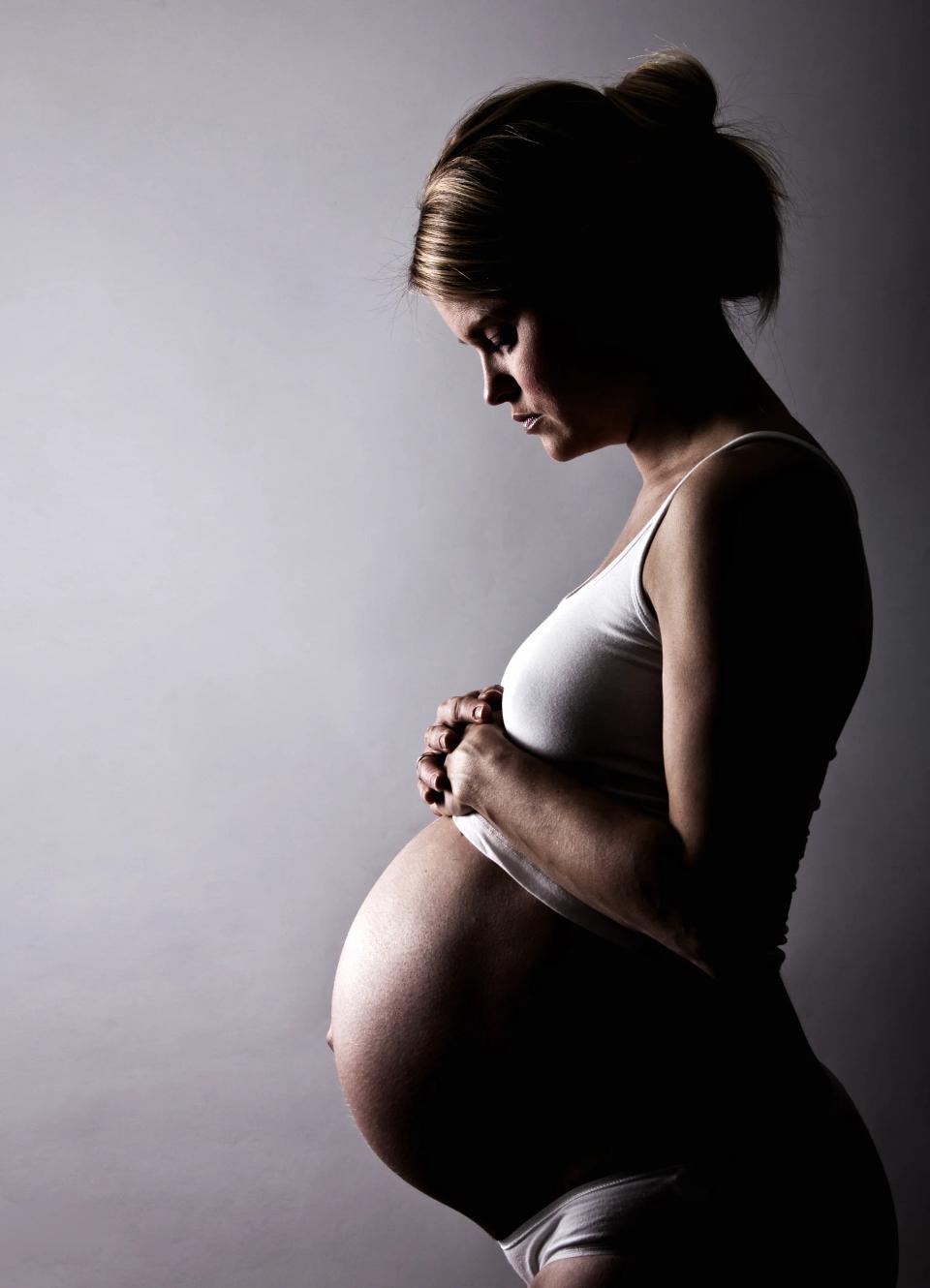 Gravid kvinde holder sin mave i profil, badet i blødt sidelys. Kontrastfuldt graviditetsfoto.