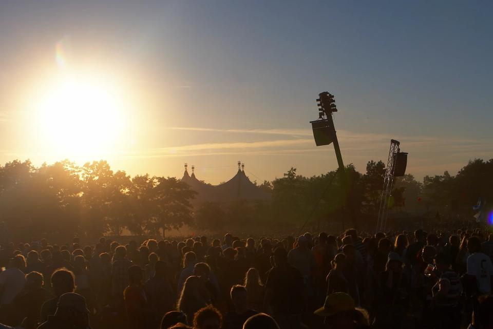 Solnedgang Roskilde Festival med orange himmel bag telt og silhuetter af publikum og træer. Fotografi i kategorien andet.